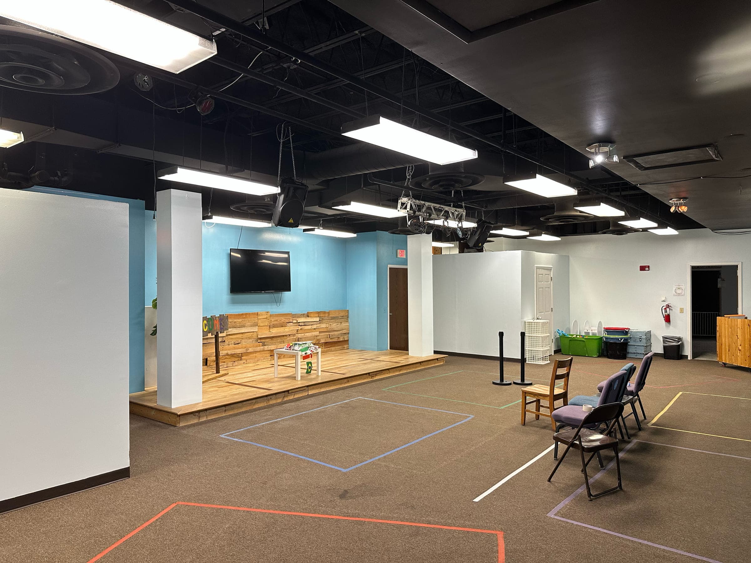 Pre-school clubhouse at Parkway Church on the Mountain in Roanoke, with a low timber stage, a reclaimed wood feature wall and an exposed ceiling carrying track lighting
