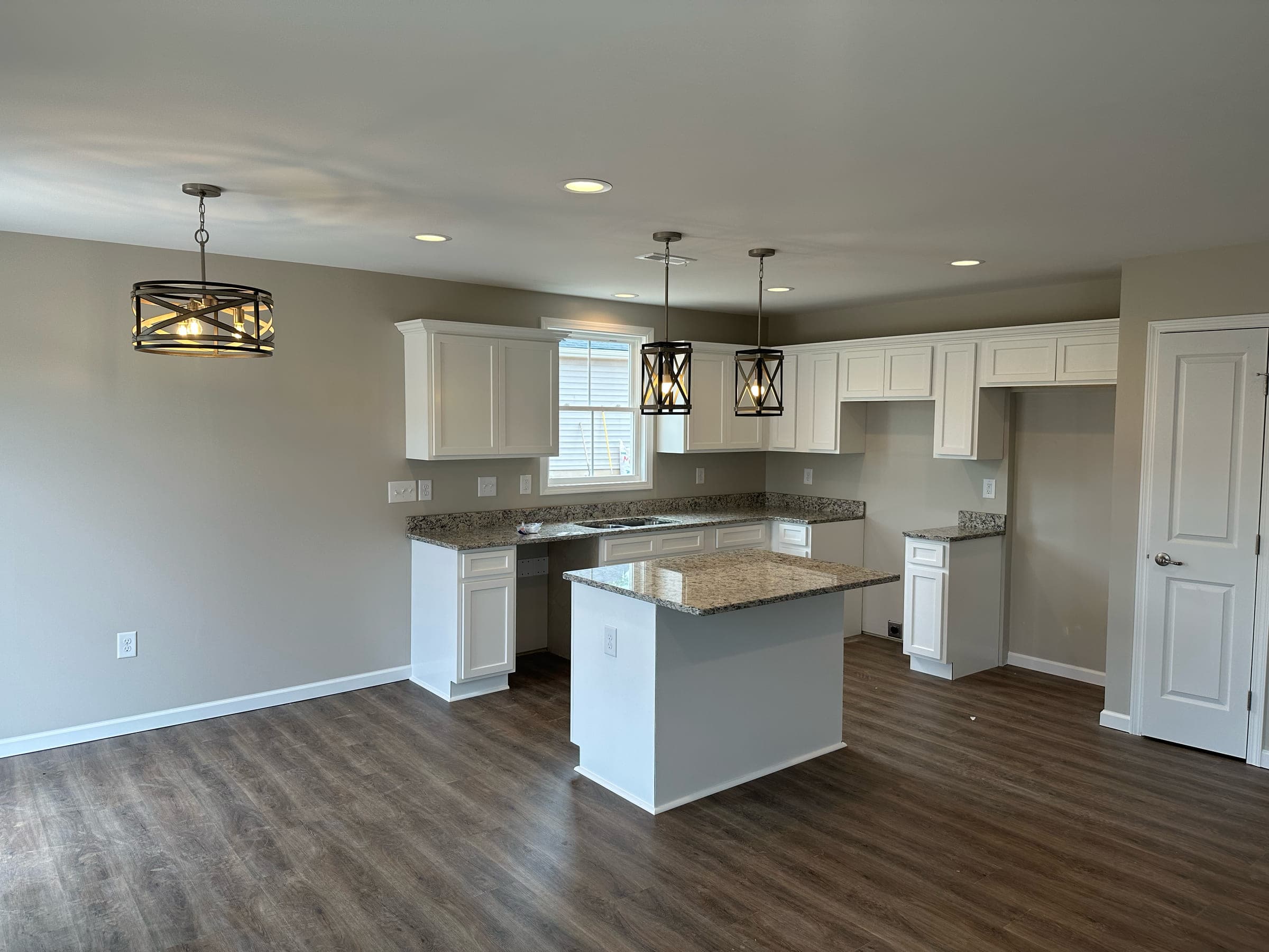 Custom home kitchen with a granite island, white cabinetry, and pendant lighting